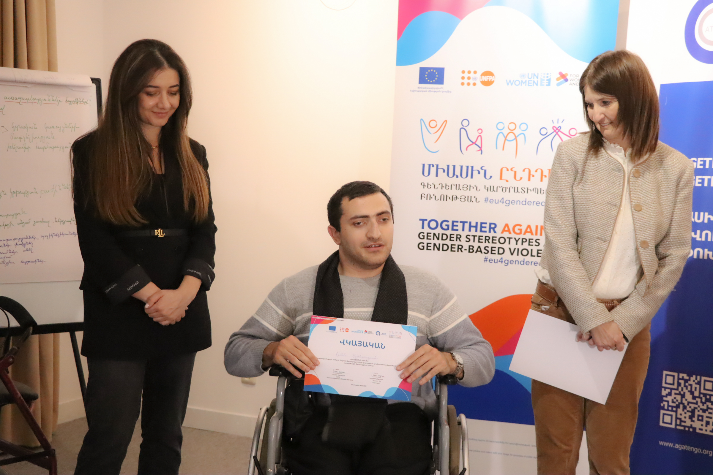 լուսանկարում Էդմոն Չիլինգարյանն է, վկայականը ձեռքին, աջ կողմում կանգնած է Կարինե Գրիգորյանը, ձախում՝ UNFP Հայաստանի ներկայացուցիչը