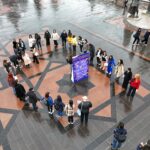 մեծ պոստեռ է, որի շուրջ հրապարակում մարդիկ շրջան են կազմել