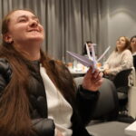 Մասնակիցներից մեկն է ժպտում է և ձեռքում պահում թողթից ճախրուկ