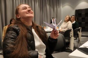 Մասնակիցներից մեկն է ժպտում է և ձեռքում պահում թողթից ճախրուկ