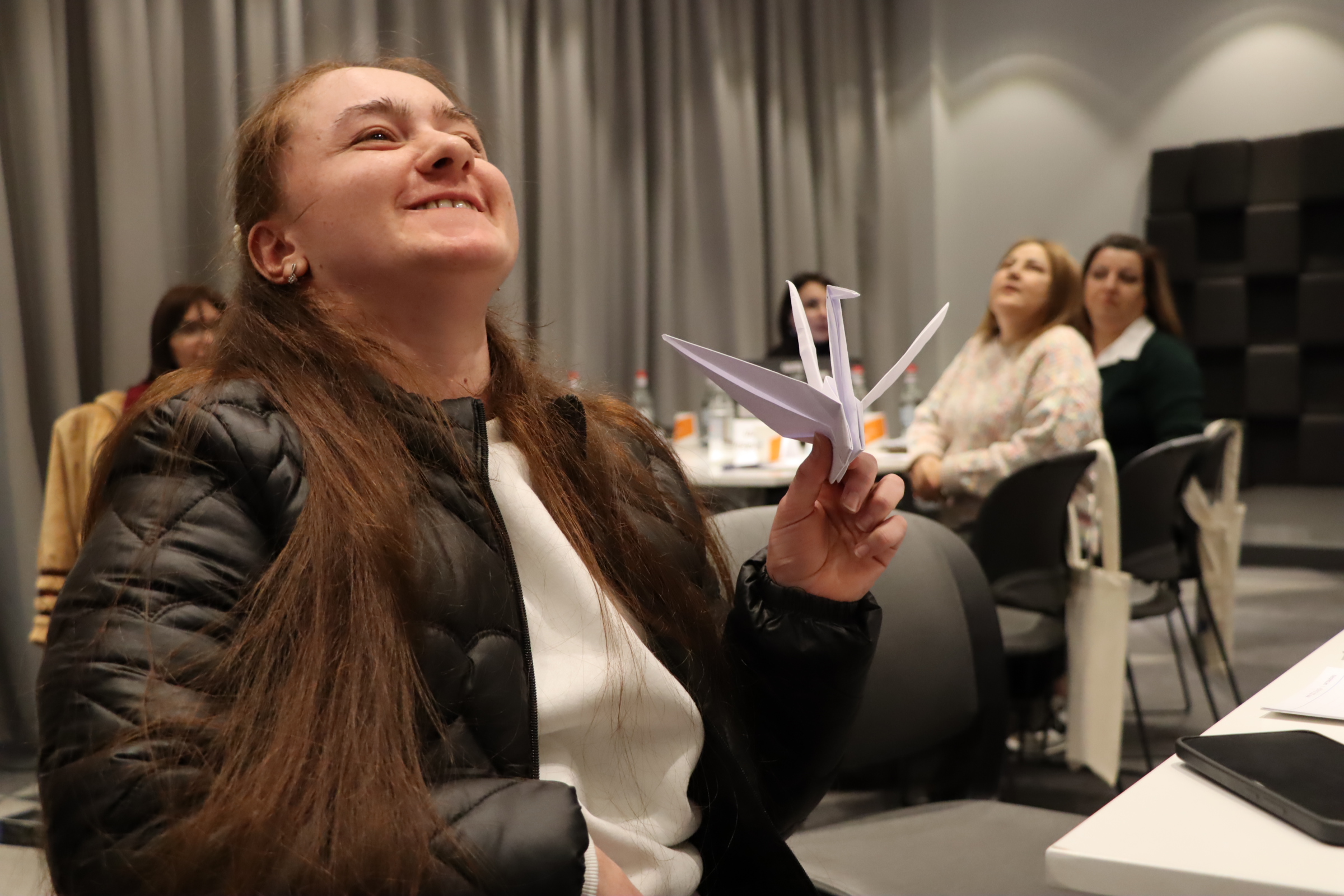 Մասնակիցներից մեկն է ժպտում է և ձեռքում պահում թողթից ճախրուկ